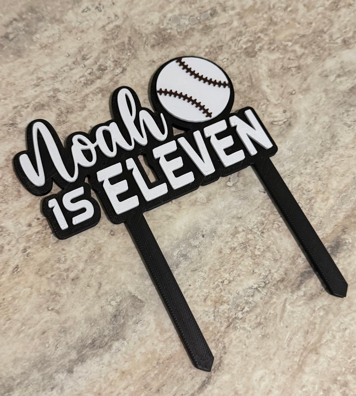 Personalized black and white 3D printed baseball cake topper reading Noah is Eleven